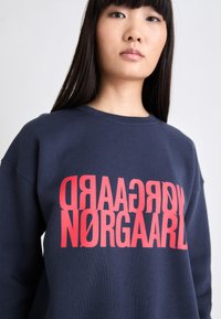 Sudadera azul marino con un corte holgado, que presenta un atrevido texto gráfico rojo. La tela tiene una textura suave y un clásico escote redondo.