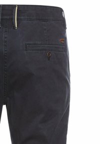 Donkerblauwe katoenen broek met een gladde textuur, voorzien van een enkele achterzak, knoopsluiting en een bruine logo-accent.