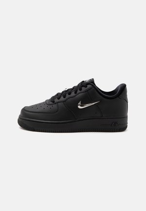 Sort lavtop sneaker fra Nike Air med sorte snørebånd, perforeret tå og sølvfarvet Nike swoosh på siden, sat mod en ensfarvet hvid baggrund.