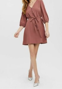 Rdzawy sukienka z dekoltem w kształcie litery V, z guzikami i wiązanym pasem. Posiada trzyczwartowe rękawy oraz luźny krój do kolan.