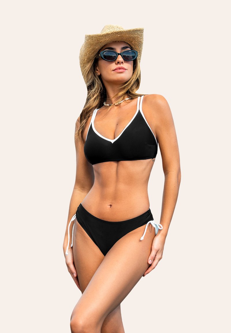 Bikini nero con dettagli bianchi, parte inferiore regolabile con lacci laterali e una texture morbida. Abbinato con un cappello da cowboy di paglia e occhiali da sole.