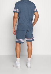 Modrá bavlněná tričko a odpovídající kraťasy s růžovými pruhovanými akcenty. Kraťasy mají rovný střih a tričko má kulatý výstřih.