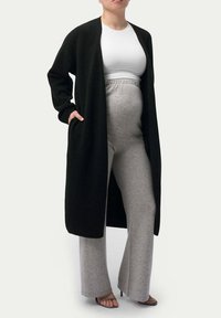 Lång svart cardigan över en vit skjorta, kombinerad med ljusgrå vida byxor. Cardiganen har fickor och ett mjukt, texturerat tyg.