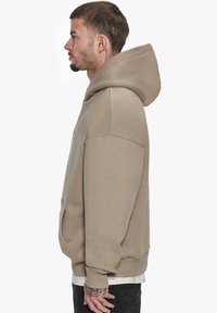 Beige hoodie med stor hætte, lange ærmer og kangaroo-lomme. Lavet af blødt stof med ribbede manchetter og kant.