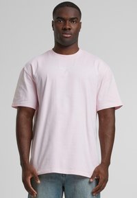 Light pink cotton t-shirt with a relaxed fit. Features short sleeves and a small embroidered logo on the chest. Smooth texture.
