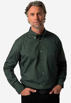 Camicia button-down verde scuro con un sottile motivo testurizzato, dotata di una tasca sul petto e colletto classico. Indossata con pantaloni neri e una cintura.