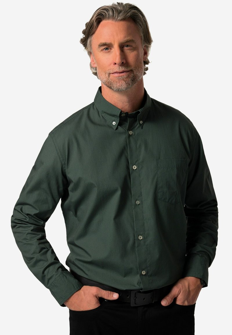 Camicia button-down verde scuro con un sottile motivo testurizzato, dotata di una tasca sul petto e colletto classico. Indossata con pantaloni neri e una cintura.