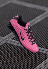 Kirik roosa ja must Nike toss mustade paeltega, mis puhkab metallvõrgust pinnal.