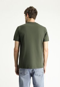 T-shirt corto a maniche corte verde oliva in misto cotone, con classico colletto girocollo e orlo dritto, abbinato a jeans di denim azzurro chiaro.