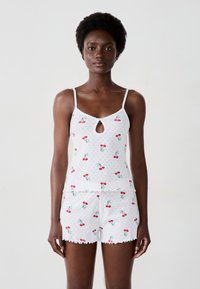 Set di pigiama in cotone bianco composto da una maglietta senza maniche con scollo a chiave e stampe di ciliegie, abbinata a pantaloni corti con bordi scallop.