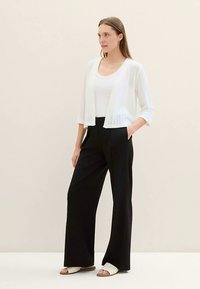 Baltas klostuotas megztinis virš balto palaidinės, derinamas su juodomis plačiomis kelnėmis ir baltais šlepetėmis. Paprastas, lengvas ir universalus aprangos derinys.