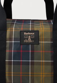 Saco tote com padrão de xadrez em verde, azul-marinho, vermelho e laranja, alças pretas e uma etiqueta preta com o texto "Barbour" e o logótipo do farol.