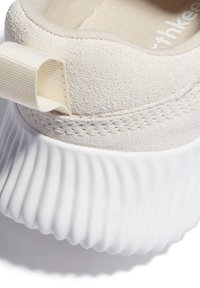 Gros plan sur le talon d'une basket beige en daim texturé, avec languette en tissu et semelle blanche épaisse rainurée.