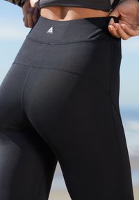 Högmidjade svarta leggings gjorda av stretchigt material, med en glatt textur, platta sömmar och en liten logotyp på midjebandet.