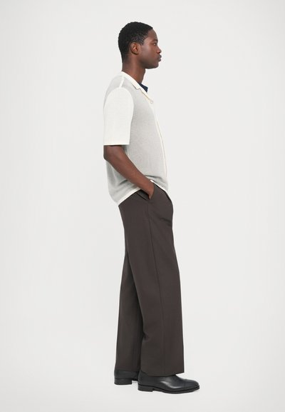 Light gray short-sleeve shirt with a textured finish, featuring a button placket. Paired with wide dark brown trousers and black shoes.