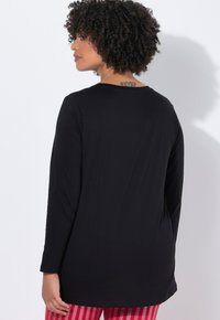 Musta pitkähiha shirts, jossa on pyöreä kaula-aukko ja sileä kangas. Takana on yksinkertainen malli ilman koristeita, yhdistettynä punaraitaisiin housuihin.