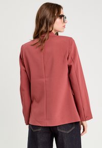 Dunkelrosa maßgeschneiderter Blazer mit Reverskragen, langen Ärmeln und geknöpften Manschetten, der einen eleganten, glatten Stoff und eine strukturierte Silhouette aufweist.