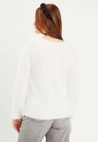 Pull blanc et fluffy avec une texture douce et des manches longues, associé à un jean en denim gris. Le bandeau est noir avec un design tressé.