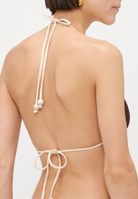 Bruine gehaakte bikini-top met crèmekleurige strikjes in de nek en op de rug, met drie decoratieve kralen aan de onderste strik. Glad, textuurstof.