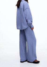 Ljusblå, texturerad oversized skjorta med långa ärmar, matchad med vida byxor i samma tyg. Svarta plattformssandaler bärs.