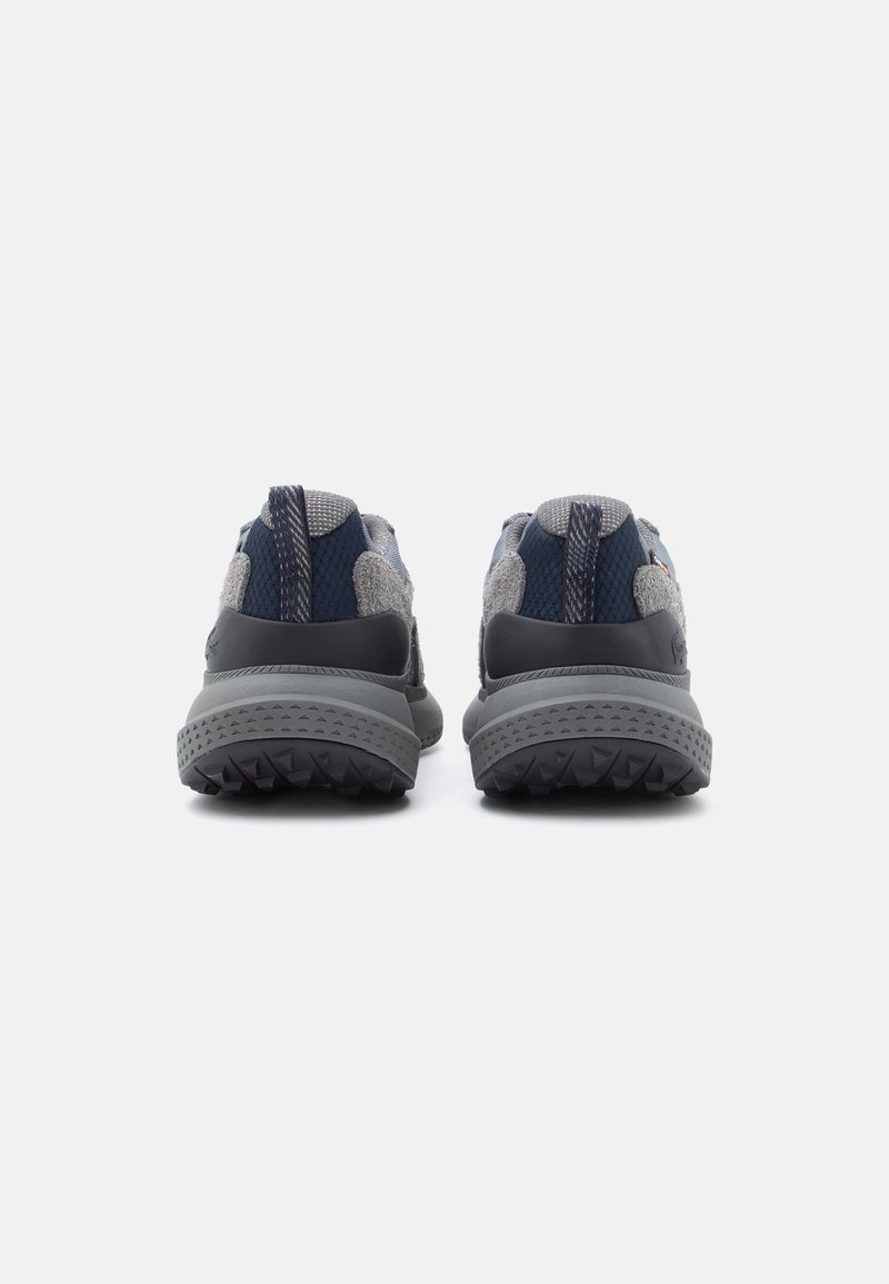 Ansicht von hinten auf Sportschuhe mit einem grauen Mesh-Obermaterial, marineblauen Akzenten und einer Gummisohle mit einem strukturierten Grip-Muster.