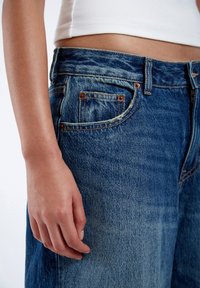 Blue denim jeans with a faded texture, featuring copper rivets, front pockets, and a slightly relaxed fit. Material appears durable and worn.