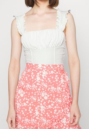 Wit, geruchte cropped top met een vierkante halslijn, gecombineerd met een roze rok met bloemmotief, met ruches en een tailleband die nauw aansluit.