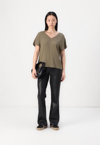T-shirt vert olive à col en V en tissu doux, associé à un pantalon en simili cuir noir et à un sac noir à la texture lisse.