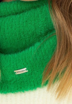 Écharpe verte en tricot duveteux avec une étiquette WITTCHEN. Présente une texture douce et un design large. Des cheveux bruns sont partiellement visibles à côté.