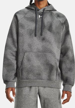 Man met een grijze, gestructureerde hoodie met voorzak en zwarte trekkoorden, gecombineerd met lichtgrijze joggingbroek.