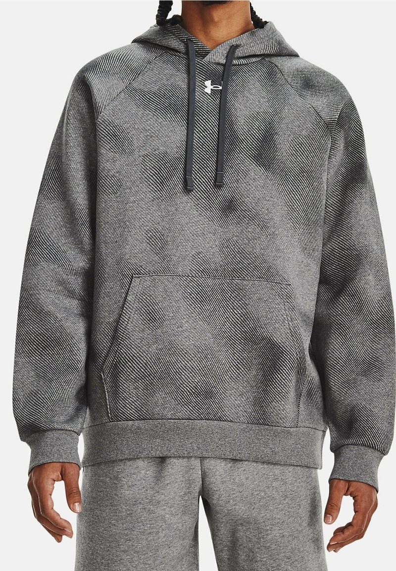 Homme portant un sweat à capuche gris texturé avec une poche avant et des cordons noirs, associé à un pantalon de survêtement gris clair.