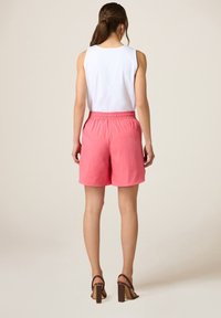 Shorts rosa con vita elastica abbinati a un top bianco senza maniche, caratterizzato da un design semplice e una texture liscia, visti da dietro.