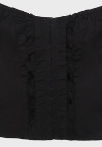 Corset en tissu noir avec bordure à volants verticale et fermeture centrale, doté d'un bord supérieur élastiqué pour un ajustement de la taille.