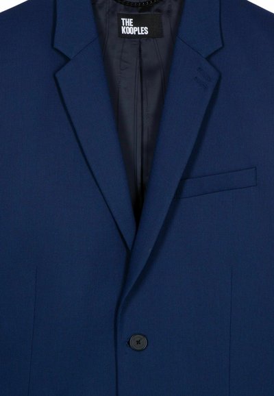 Marineblauer Blazer aus strukturiertem Stoff, mit tiefem Revers, einem einzelnen schwarzen Knopf und einer Brusttasche. Innenfutter sichtbar.