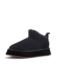 Botines de ante negro con un suave forro de piel. Presentan una puntera redondeada, detalles de costura y una suela plana de goma.