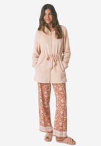 Tan blomster fleecejakke med snoreliv, parret med orange mönstrede bredbenede bukser og lyse, fuzzy slippers.
