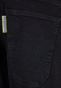 Un bolsillo de denim negro con una etiqueta amarilla y azul a rayas etiquetada como "homeboy". Presenta costuras visibles y un diseño en forma de diamante en el bolsillo.