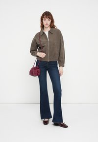 Veste en velours côtelé vert olive avec fermeture éclair sur le devant, taille élastique et deux poches avant, associée à un jean bleu évasé et un sac bandoulière bordeaux.