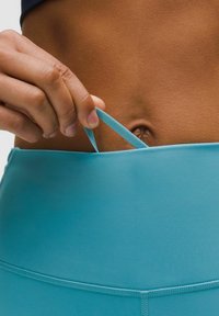 Tirkīza sporta josta ar gludu tekstūru. Roča pievilk blue aukliņu no jostas. Tuvplāns uz ādas toni un auduma detaļām.