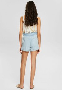 Light denim shorts with an elastic waistband, frayed hem, and a relaxed fit, paired with a striped sleeveless top.