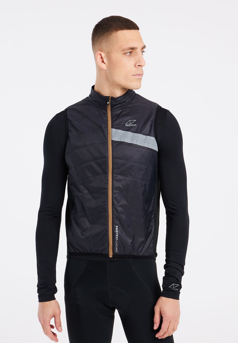 Sort quiltet vest med lynlås fortil og grå refleksstribe; har logo og teksturerede paneler. Bæres over en sort langærmet top.