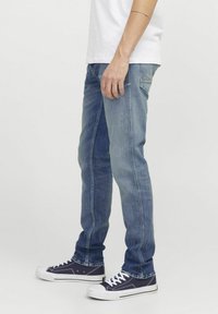 Jean en denim bleu clair avec une coupe slim, présentant des coutures contrastées, un design à cinq poches, et associés à des baskets bleu foncé.