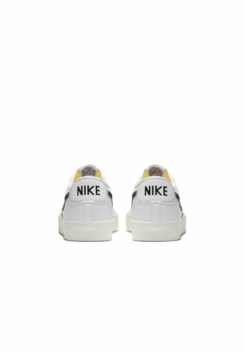 Sneaker bianche con tomaia in pelle liscia, dettagli neri, interno giallo e grande logo "NIKE" sul tallone.