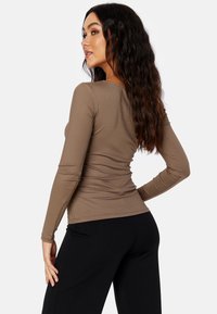 Braunes, geripptes Langarmoberteil mit figurbetontem Schnitt, rundem Halsausschnitt und gerafften Details an der Taille, kombiniert mit schwarzen Hosen.