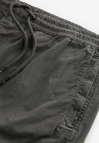 Dunkelgraue Shorts aus leichtem Stoff mit elastischem Bund, Kordelzug und einer Reißverschlusstasche. Glatte Textur, minimalistisches Design.