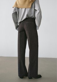 Donkere bruine broek met wijde pijpen van gestructureerde stof, met een hoge taille en subtiele achterzakken, gecombineerd met een grijs shirt met lange mouwen.