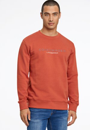 Sweatshirt couleur rouille avec un col rond et des manches longues, arborant le texte "COPENHAGUE LINDBERGH" en gris sur la poitrine.
