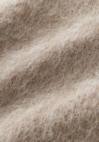 Close-up of soft, fuzzy beige fabric with fine, curly fibers and gentle folds creating texture and depth.