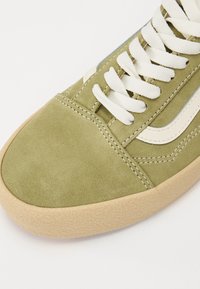 Baskets en daim vert avec des lacets crème. Elles présentent une semelle en gomme texturée, une bande latérale blanche contrastante et des détails de couture blanche.