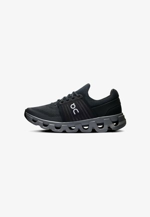 Black athletic shoes with a breathable mesh upper, textured dark accents, and a unique wavy sole design. Features logo on side.